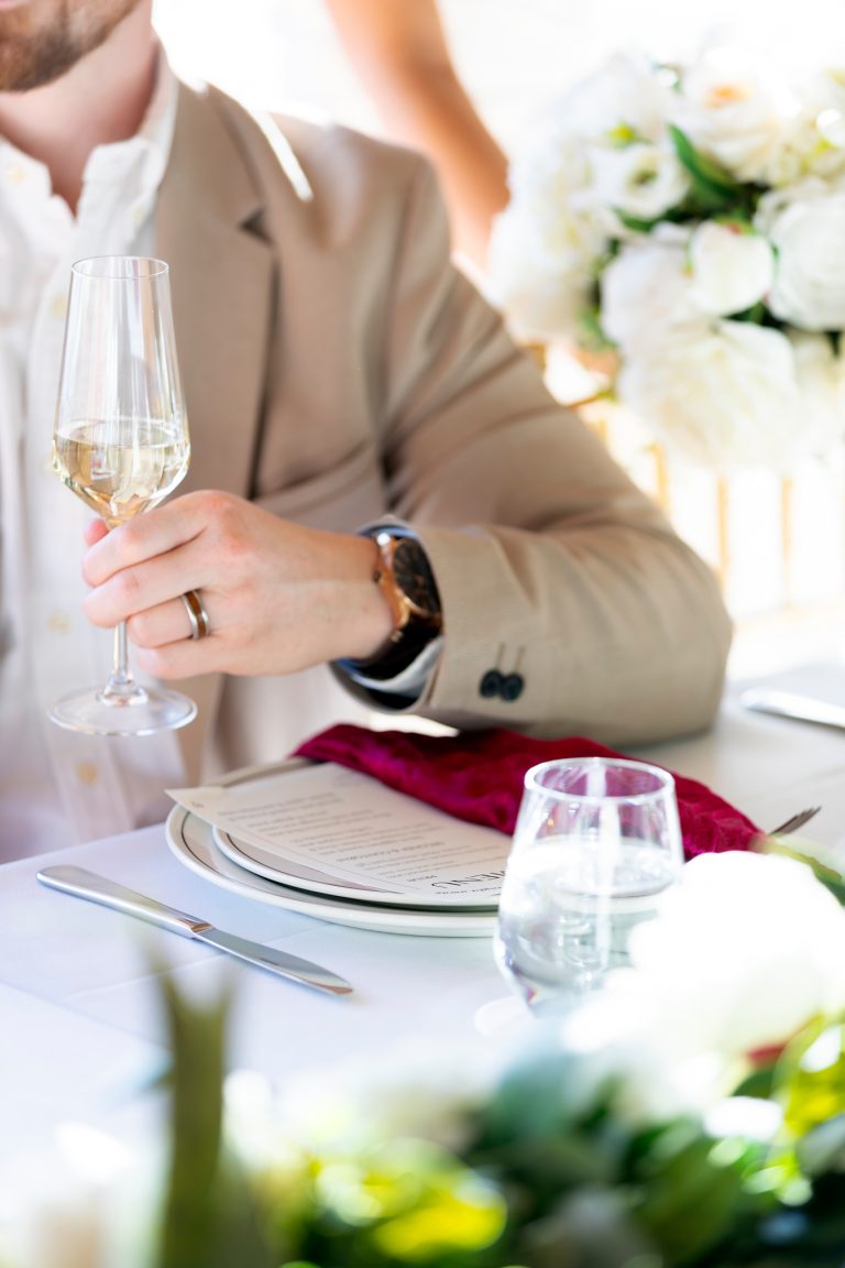 Champagne detail at a wedding table set with white florals and tall candlesticks