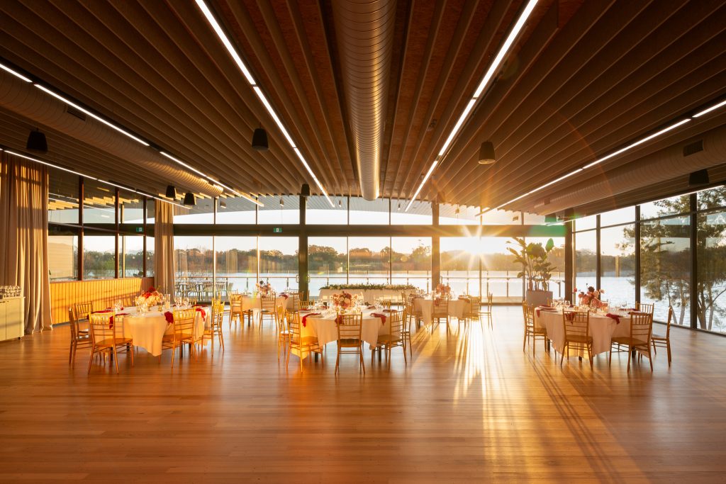 The Telopea Room at sunset, sun flaring through the glass wall over a dressed wedding reception
