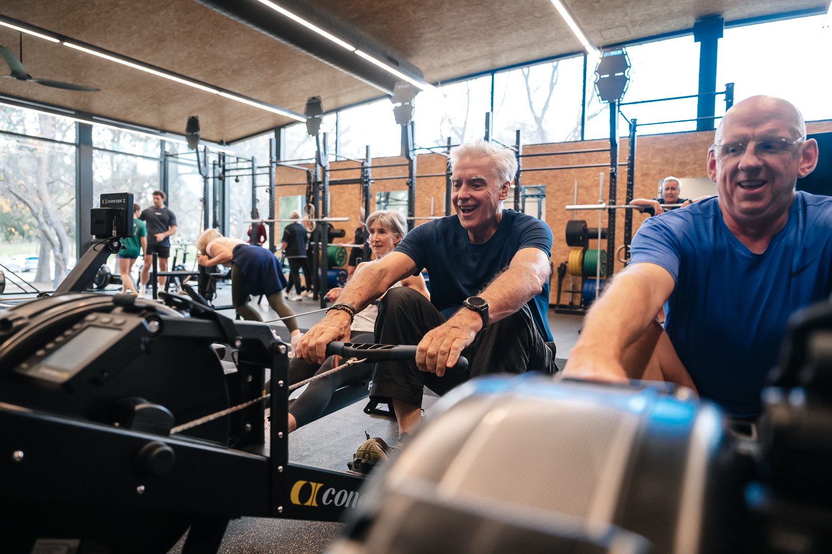 Member laughing mid rowing-machine stroke in a busy class