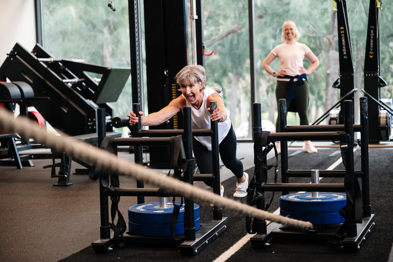 Member grinning mid sled push with a smiling trainer at RSX