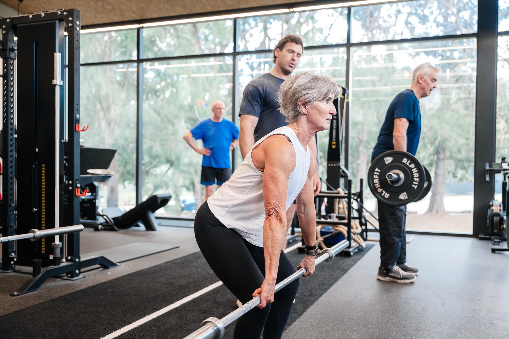 Member deadlifting while a trainer checks her form