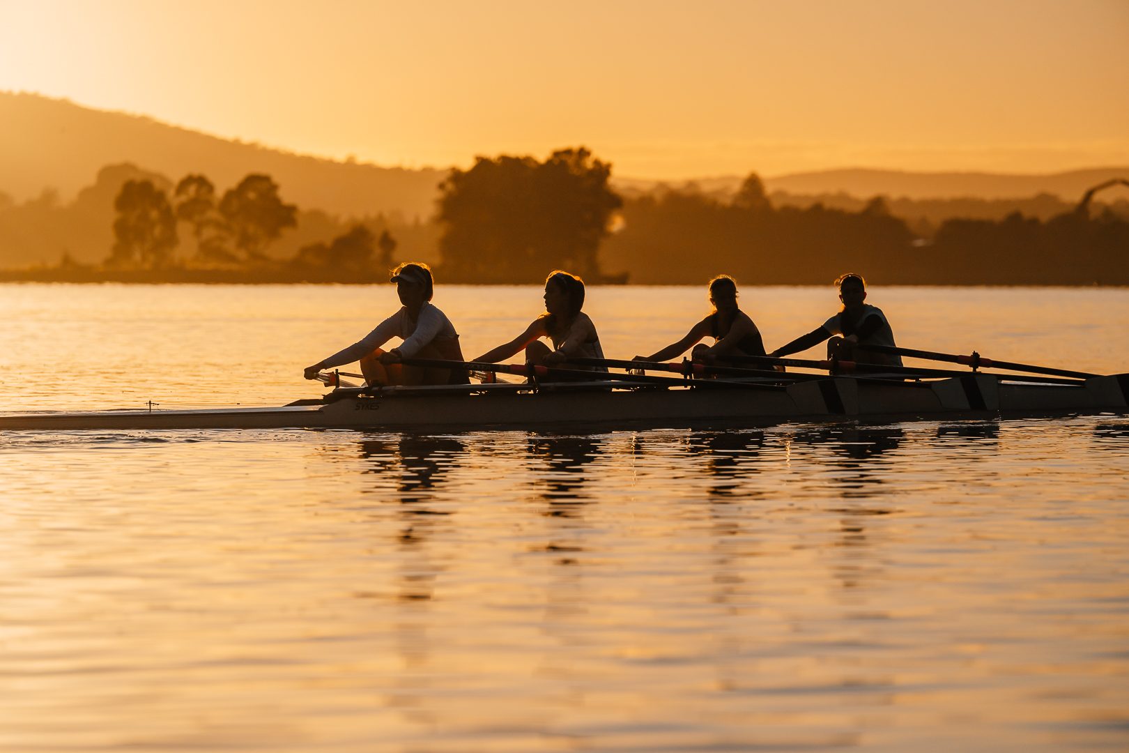 Crew rowing through apricot dawn mist on Lake Burley Griffin