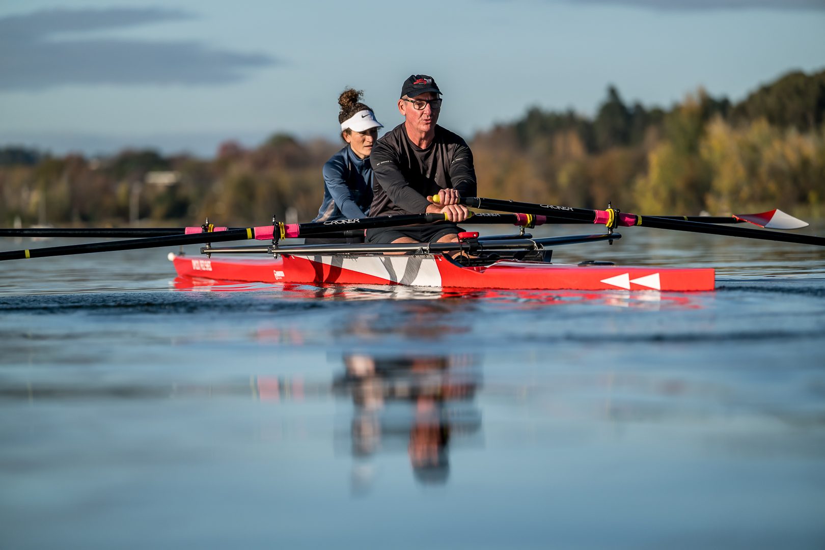 Mixed-age double scull mirrored on still blue water