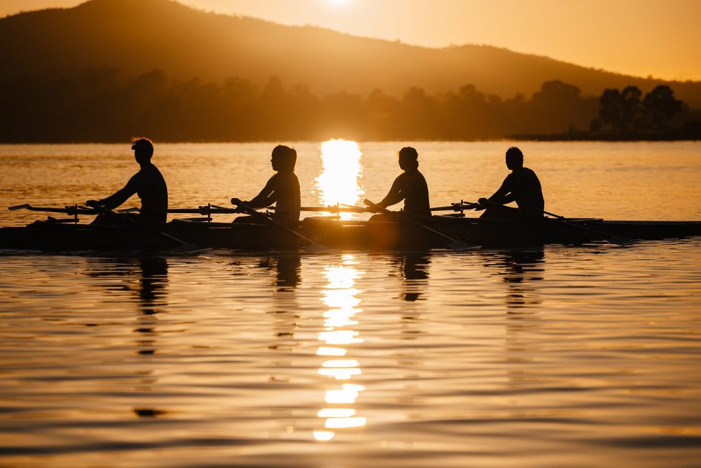 Four rowers silhouetted in perfect sync at sunrise on Lake Burley Griffin