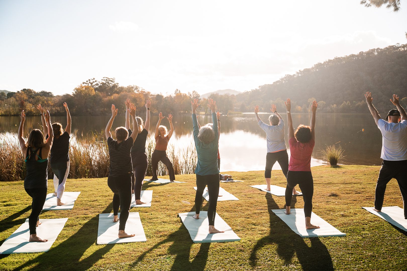 Yoga class reaching skyward together beside the lake at golden hour