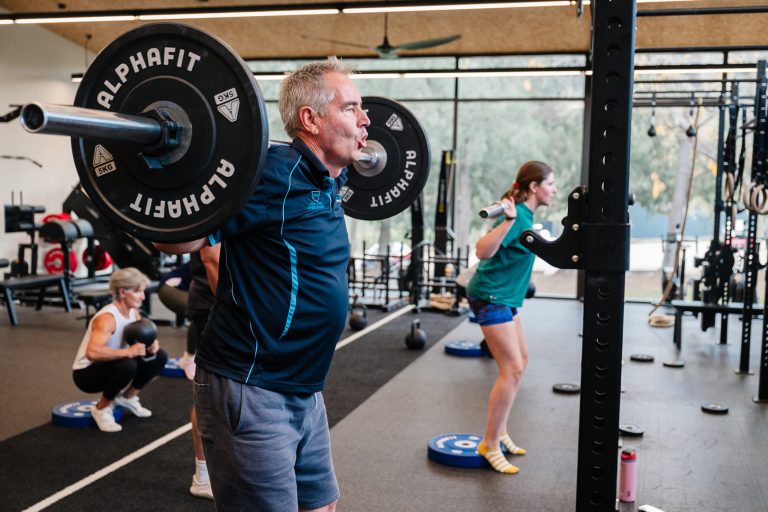 Member front squatting a barbell while others train alongside at RSX