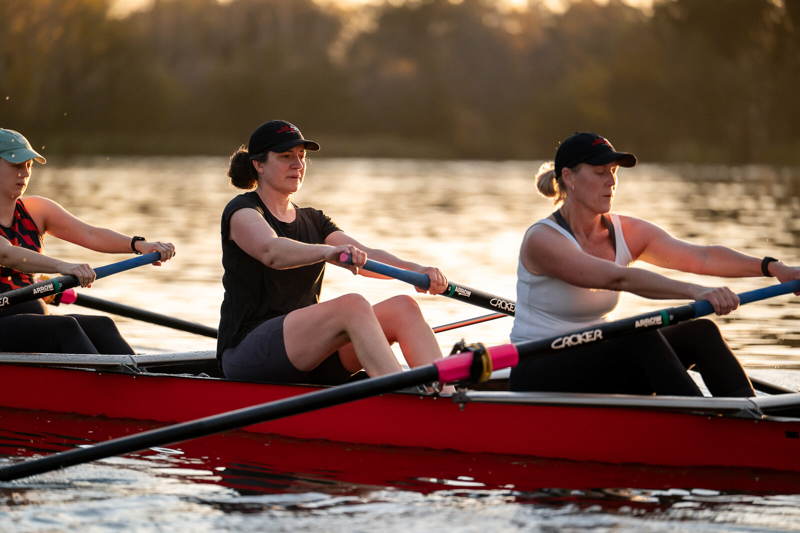 Masters crew rowing a red Red Shed quad on Lake Burley Griffin at golden hour