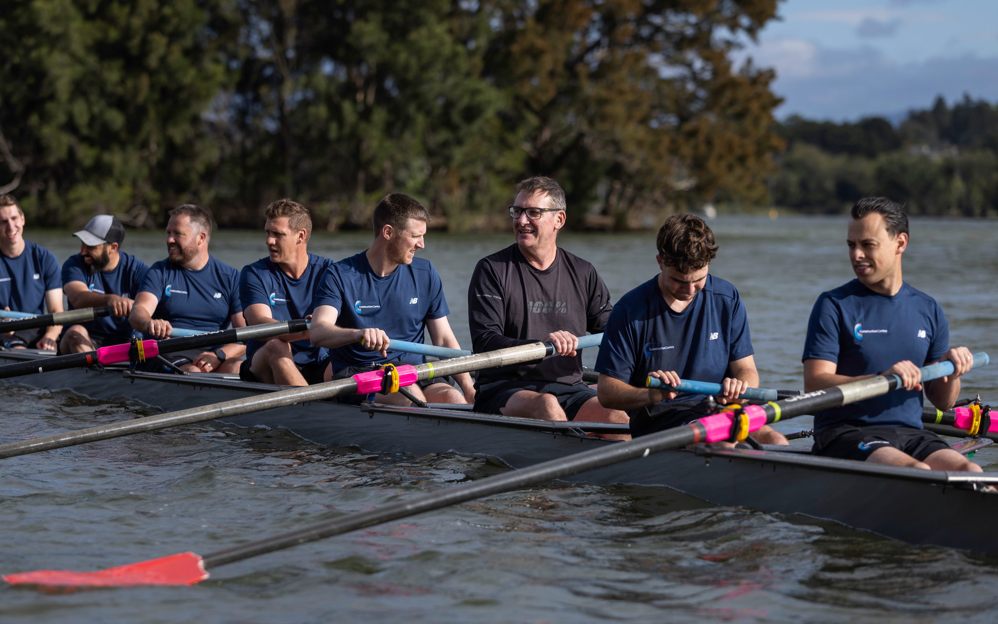 A smiling corporate crew in the sun after rowing on the lake