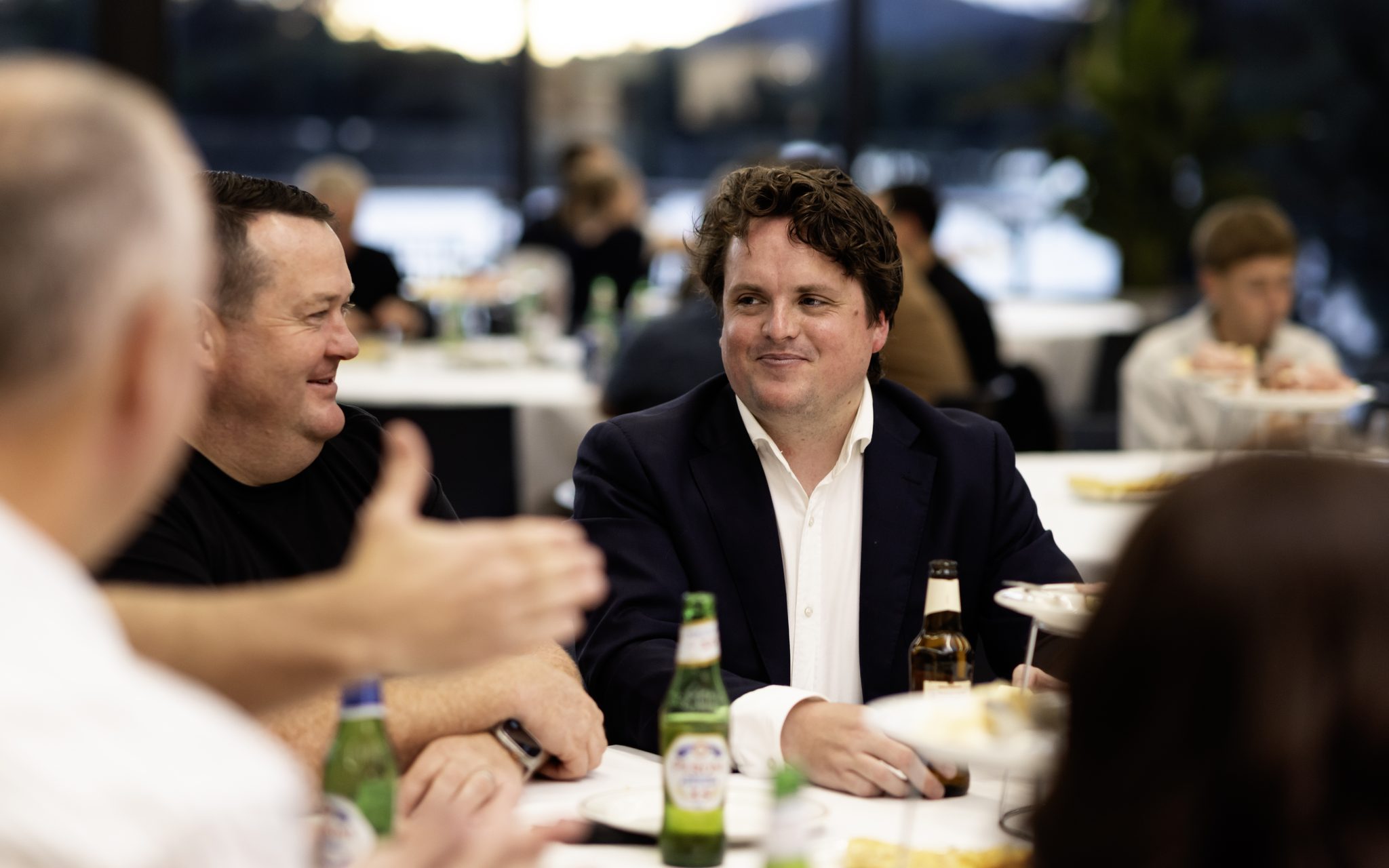 Corporate guests laughing over dinner beside the lake windows