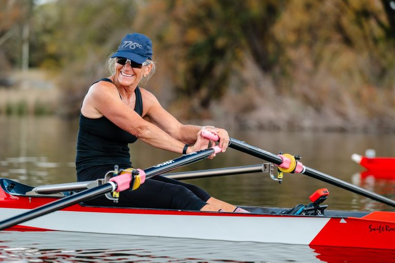 Rower laughing in a red and white single scull on the lake