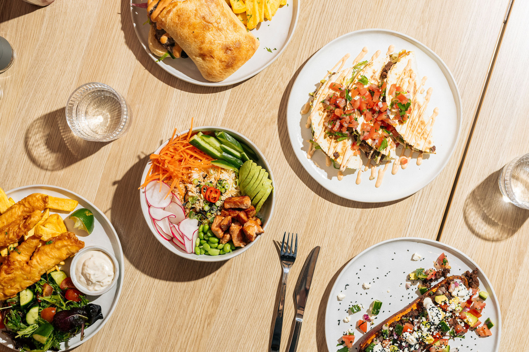 Overhead view of lunch at Easy Oar: fish and chips, a grain bowl and a cold drink