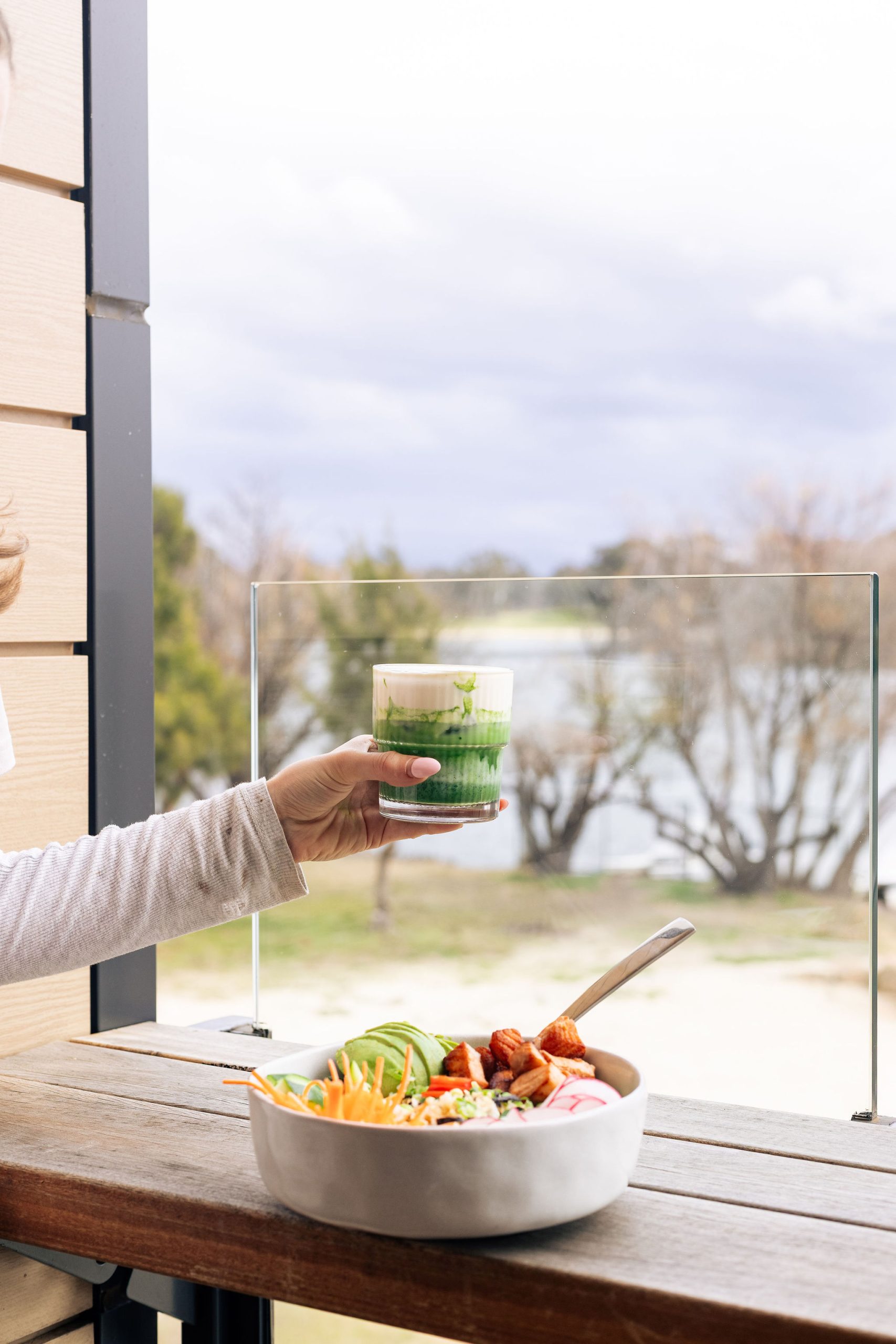 A green drink held at the window ledge with the lake and trees beyond