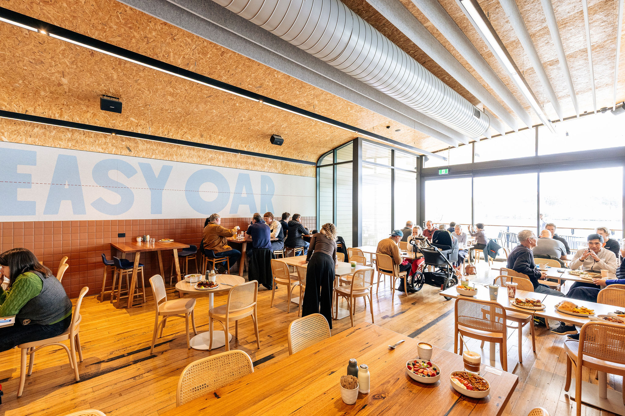 A full Easy Oar Cafe with people at timber tables beneath the Easy Oar mural