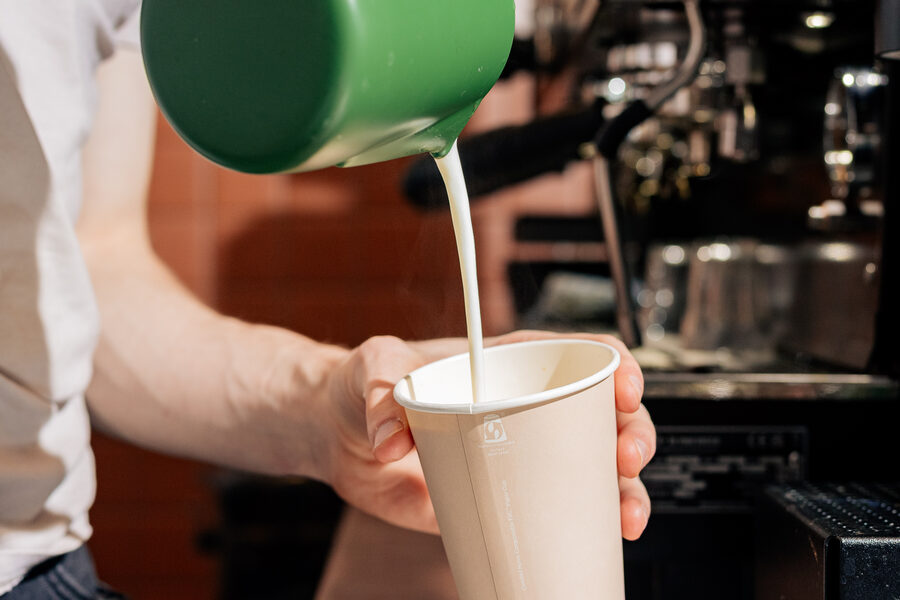 Barista pouring steamed milk from a green jug into a takeaway cup at Easy Oar