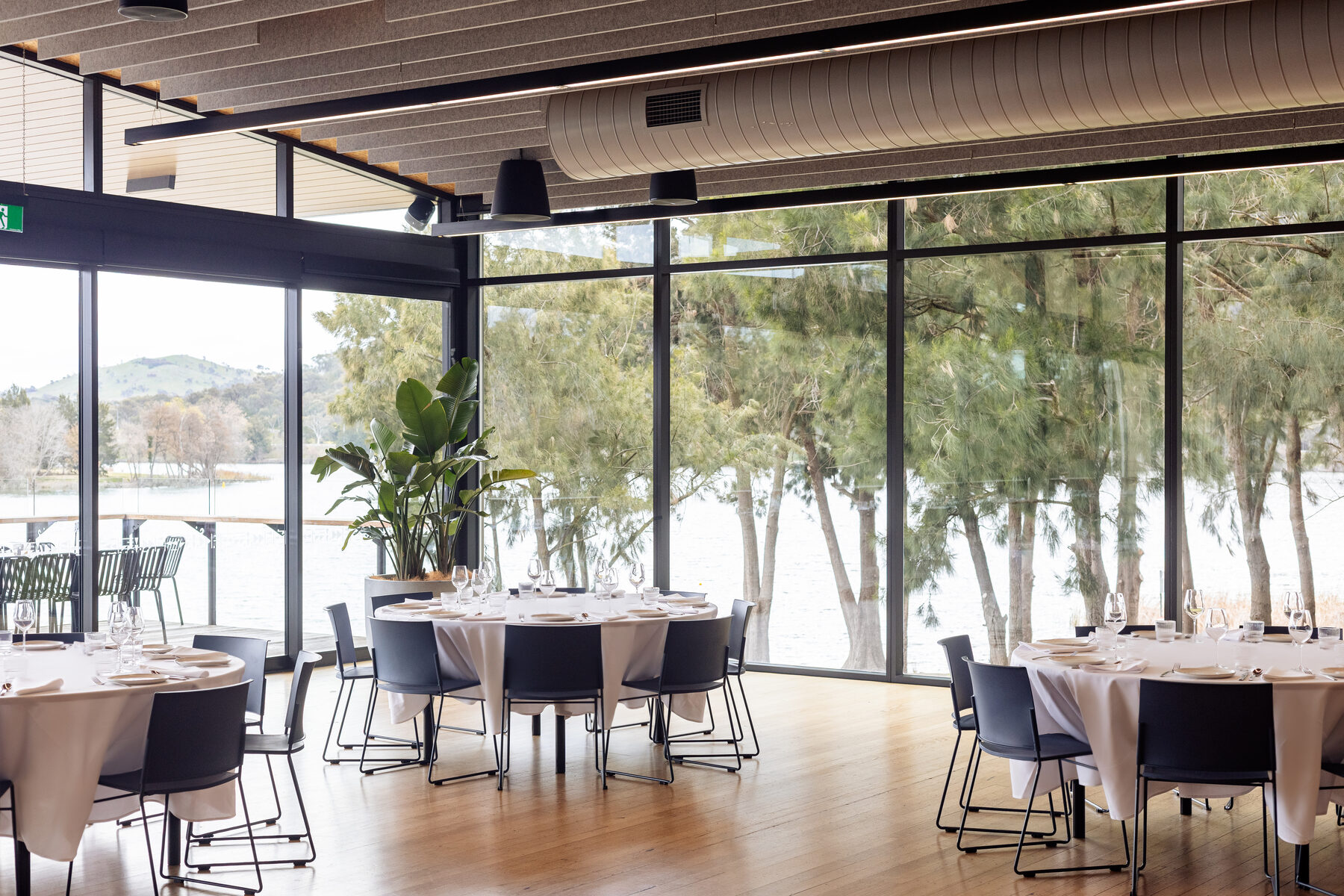 The Telopea Room set with round tables and white linen for a function, lake through the windows